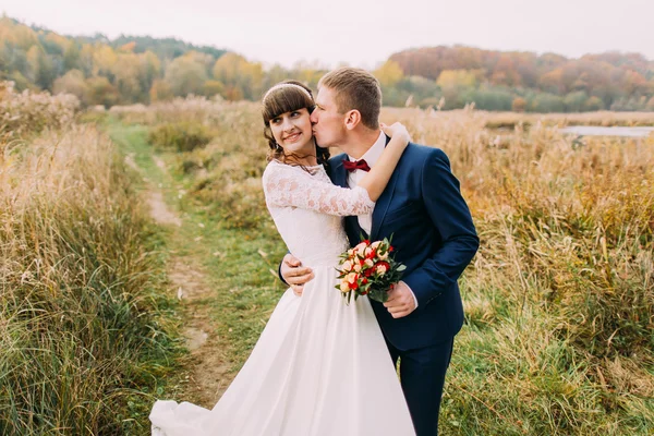 Güzel yeni evli genç çift açık havada portresi. Şık damat büyüleyici gelini öpüşme — Stok fotoğraf
