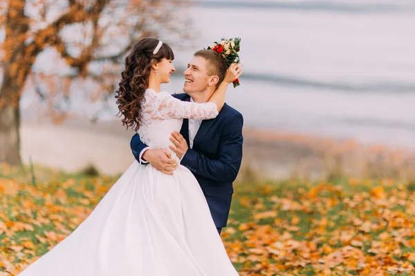 Gelukkig jonge kersverse bruidspaar poseren op herfst lakeshore vol met oranje bladeren — Stockfoto