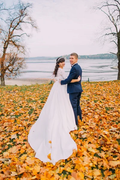 Šťastný mladý čerstvě ženatý, pár pózuje na podzimní jezera plná pomerančové listí — Stock fotografie
