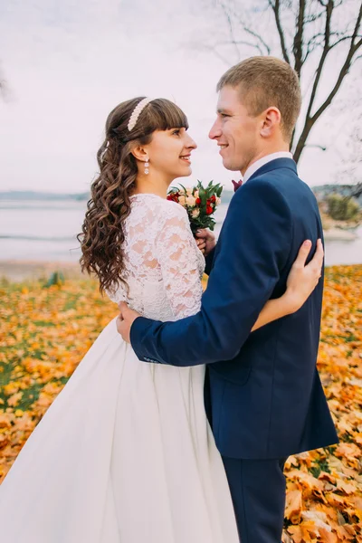 Retrato de feliz joven pareja recién casada posando en otoño orilla del lago hojas naranjas completas —  Fotos de Stock