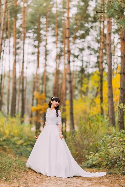 Belle jeune mariée brune innocente en magnifique robe blanche se tient sur le sentier de la forêt — Photo
