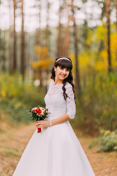 Vackra oskyldiga unga brunett brud i klassisk vit klänning står på skog spår — Stockfoto