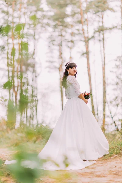 Hermosa inocente joven novia morena en vestido blanco magnífico se encuentra en el sendero del bosque en el día soleado —  Fotos de Stock