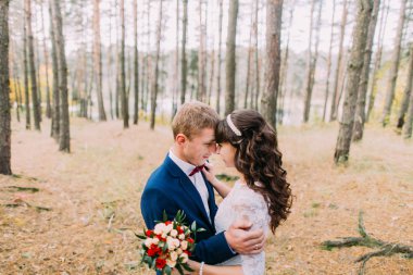 Mutlu şık damat ve sonbahar çam ormanı içinde poz büyüleyici yeni eşi