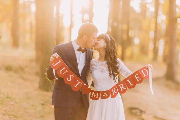 Glücklicher romantischer Bräutigam und seine charmante neue Frau mit frisch verheirateten Schild im sonnigen Wald — Stockfoto