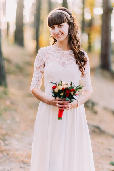 Linda noiva jovem morena inocente em vestido branco lindo com buquê de flores na floresta — Fotografia de Stock