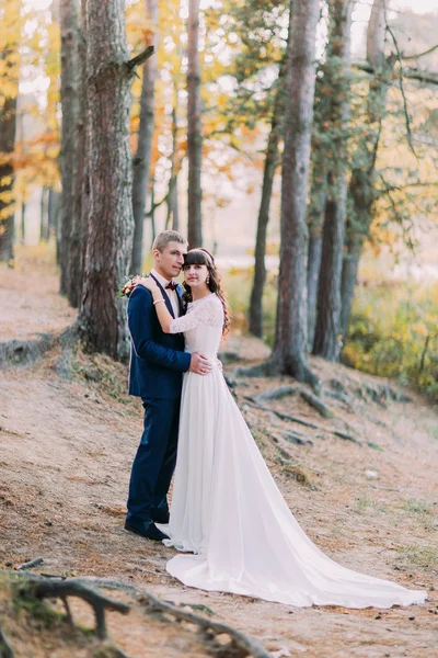 这对新婚的夫妇互相抱着。散布在森林地面上的新娘长裙尾 — 图库照片