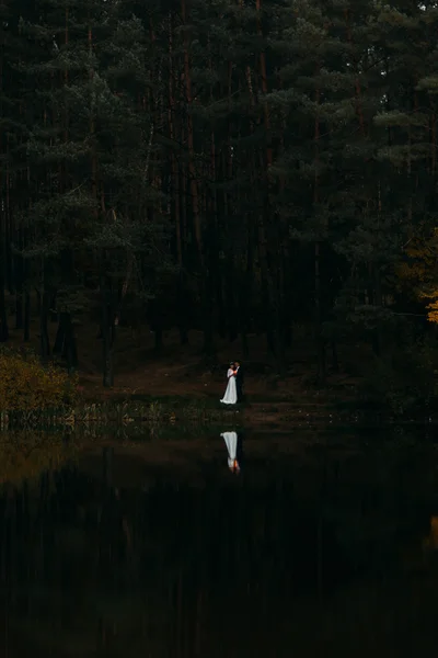 Novio y su encantadora nueva esposa besándose en la orilla del lago del bosque en la noche oscura — Foto de Stock