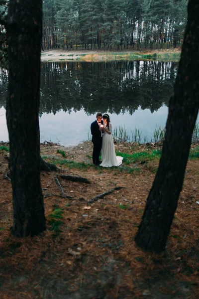 Novio y su encantadora esposa besándose en la orilla del lago del bosque sosteniendo vela ardiente en la noche — Foto de Stock