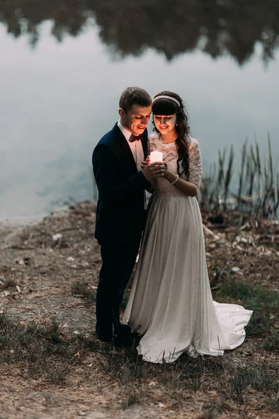 Damat ve akşam saatlerinde Orman Gölü kıyısında bir mum tutan büyüleyici yeni eşi — Stok fotoğraf