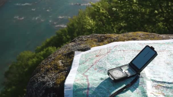 Современный компас с картой местности на выветриваемом камне возле широкого горного потока — стоковое видео