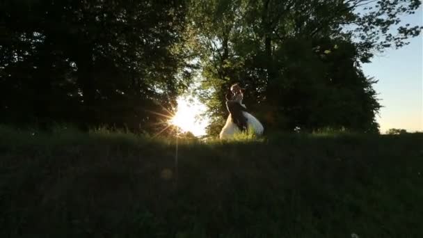 Beau couple de mariage s'amuser. Mariée et marié riant et tournant dans la forêt verte. Merveilleux coucher de soleil sur le fond 