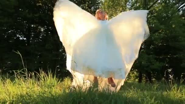 Atractiva novia rubia joven saltando y divirtiéndose en el prado verde en el soleado día de verano — Vídeos de Stock