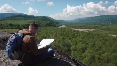 Dağ taş üzerinde otururken kontrol manzara arazi harita ile aktif genç adam