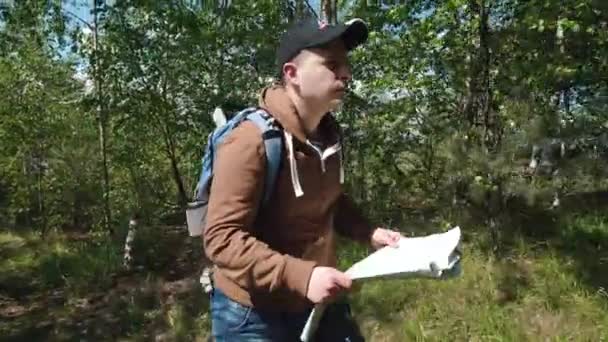 Young active man walking through highland forest and checking his way with paper terrain map — Stock Video