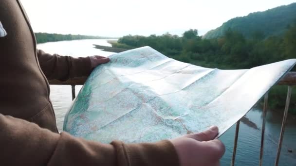 Νεαρός τουριστικά ελέγχοντας τον τρόπο του σε διαδρομή με χάρτη όταν περπατάτε στη γέφυρα στα βουνά — Αρχείο Βίντεο
