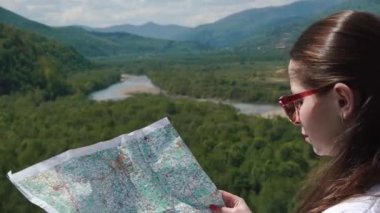 Genç kadın güneş gözlüğü cheking onu harita ayakta highland ile nehir manzara olumsuz yönü ile
