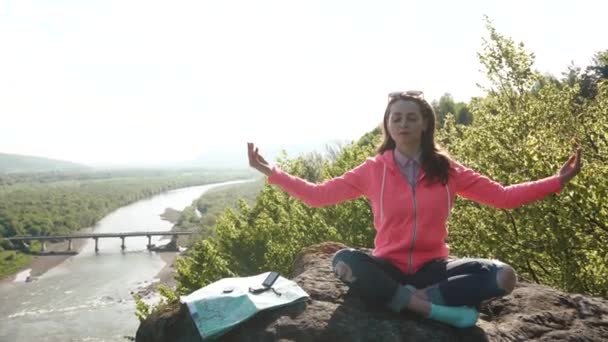 Giovane ragazza attiva si rilassa praticando yoga a roccia di montagna. Ampia valle del fiume come sfondo — Video Stock