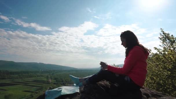 Retrato de una mujer joven descansando en la pendiente de la roca y mirando el dispositivo de navegación en sus manos — Vídeo de stock