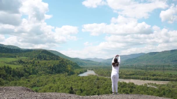 Giovane donna in piedi sul bordo delle colline e che estende il suo corpo sotto magnifico cielo limpido — Video Stock