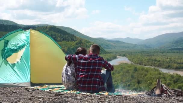 Mladí turistické pár objímat v kempu s ohněm na skalnatý vrchol kopce v zelené hory — Stock video