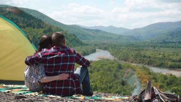 Casal de turistas romântico abraçando no local do acampamento com fogueira no topo rochoso da colina em montanhas verdes — Vídeo de Stock