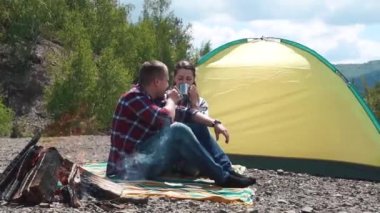 Genç turist iki kayalık üst kısmındaki yeşil dağların Hill'de ateşin ortasına ile Kamp yerinde. Güzel kız gülümsüyor sonra erkek omzuna elini koyar