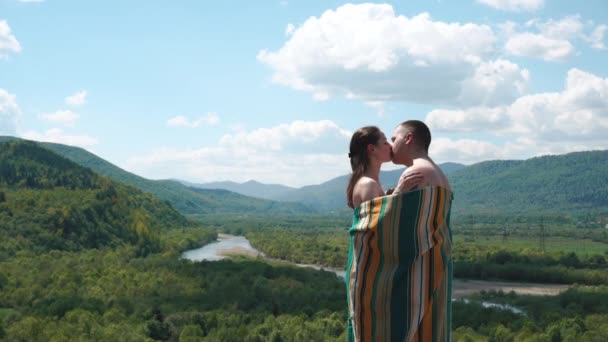 Молодая пара, покрытая подкладкой, держит друг друга на вершине холма с удивительным видом — стоковое видео