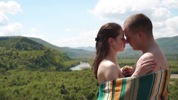 Pareja joven cubierta de manta forrada sosteniéndose unos a otros en la cima de la colina con una increíble vista de la colina del bosque — Vídeo de stock