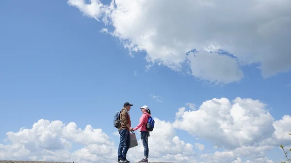 Щаслива туристична пара з рюкзаками тримає руки на фоні хмарного неба — стокове фото