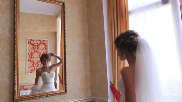 Невеста смотрит на себя в зеркало, примеряет свадебное платье утром в день свадьбы — стоковое видео