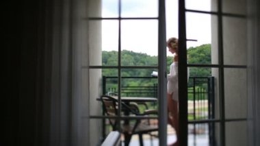 Onun kitap üzerinde balkon ve gülümsüyor, sabah ışık beyaz bluz rahat kadın okur