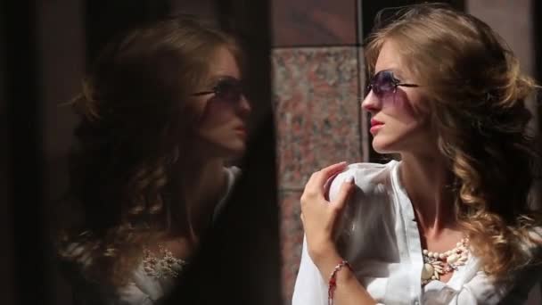 年轻漂亮微笑的女人在太阳镜和白色衬衫与热轧的 sveeves 站在附近的现代城市的建设大理石柱阳光 — 图库视频影像