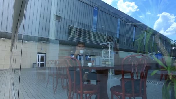 Uomo d'affari che beve caffe 'nero, seduto in un caffe' luminoso. Vista dalla grande finestra di mirroring — Video Stock