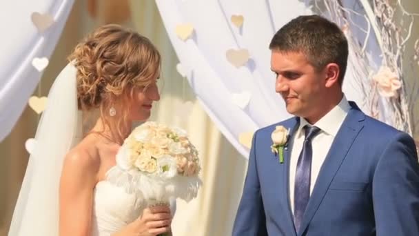 Beautiful young couple, bride and groom, standing and talking near wedding arch after the ceremony — Stock Video