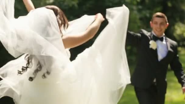 Jeunes mariés - mariés posant ensemble et s'amusant. Élégant marié joue avec le voile nuptial, et ils rient tous les deux. Plan extérieur avec parc d'été comme arrière-plan 