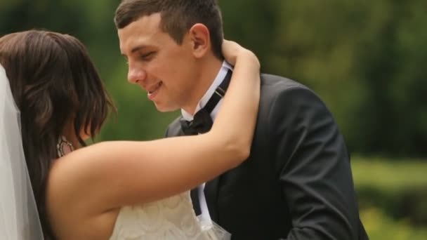 Joyeux jeunes mariés embrassant, dans le parc vert d'été. beau marié incline doucement et embrasse sa belle mariée — Video