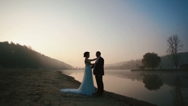 Dva šťastní novomanželé všeobjímající na večerní svatební den na romantická jezera na západ slunce — Stock video