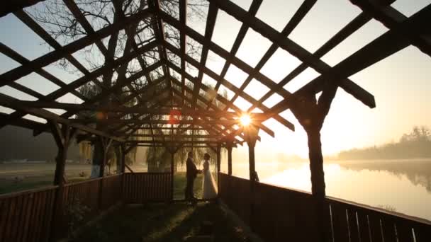 Romantique paire de jeunes mariés embrassant à la porte du hangar de plage le soir du jour du mariage près du lac de villégiature de montagne sur le coucher du soleil — Video