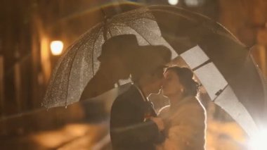 Güzel noir tarzı çift kisssing gece şehir sokak, yağmur şemsiye altında saklanıyor yağmur altında