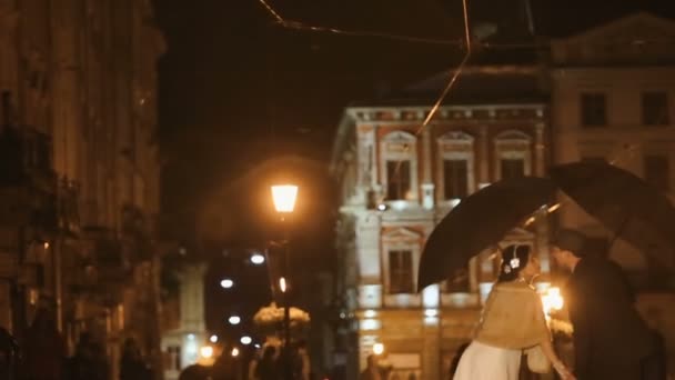 Par klädda i noir retro kostymer kyssas under regn på natten staden street, gömmer sig från regn under paraplyer — Stockvideo