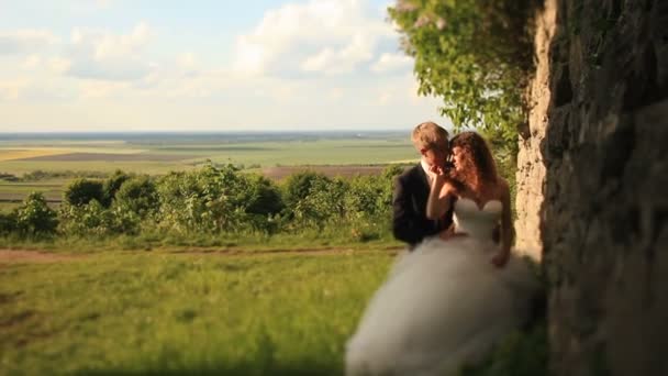 Όμορφος groom κατέχει με αγάπη την όμορφη νύφη ενώ αγκαλιάζουν την στέκεται κοντά σε παλαιό ερειπωμένο τοίχος — Αρχείο Βίντεο