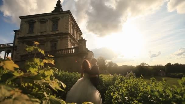 Romantischer Moment des frisch vermählten Paares im Sonnenuntergangspark in der Nähe des historischen Palastgebäudes — Stockvideo