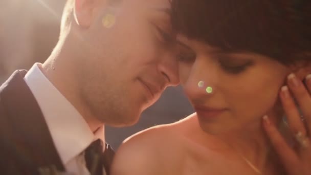 Close-up de jovens recém-casados casal sorridente. Bonito noivo gentilmente tocando sua noiva encantadora em luzes de pôr do sol — Vídeo de Stock