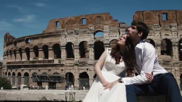 Hochzeitspaar in Rom am Kolosseum nebeneinander sitzend und einander umarmend. Flitterwochen in Italien, Europa — Stockvideo