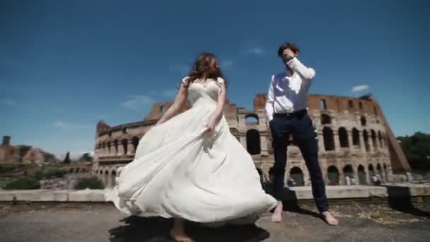 Pareja de boda en Roma por el Coliseo, novio feliz ve a su novia bailando en su vestido de novia largo. Luna de miel en Italia, Europa — Vídeos de Stock