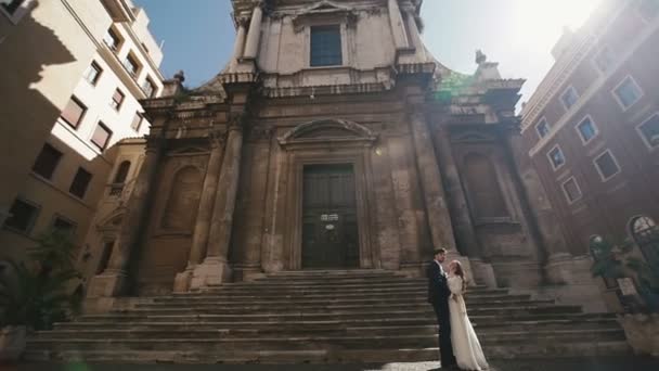 Sposi a Roma che si baciano vicino alla chiesa di San Nicola da Tolentino. Bella sposa ed elegante sposo delicatamente ebraces. Luna di miele in Italia, Europa — Video Stock