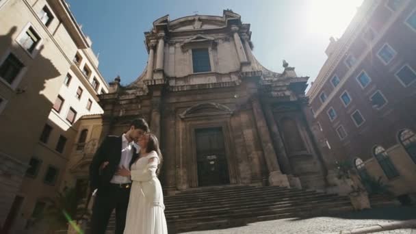 サン ニコラ ・ ダ ・ トレンティーノ教会を付近のローマのキスで結婚式のカップル。美しいスタイリッシュな新郎新婦 ebraces 優しく互い。イタリア、ヨーロッパの新婚旅行 — ストック動画
