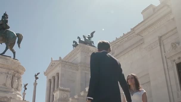 Весільний пара у Римі позує перед Altare делла Patria в Римі, Італія. Стильний нареченого прогулянки навколо красиві нареченої hlding її за руку. Медовий місяць в Італії, Європа — стокове відео