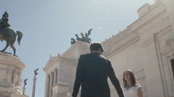 Coppia di sposi a Roma in posa davanti all'Altare della Patria a Roma, in una giornata di sole. Elegante sposo cammina intorno bella sposa tenendo la mano. Luna di miele in Italia, Europa — Video Stock